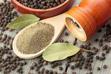 Wooden pepper mill, laurel leaves, black peppercorns and ground black pepper on old wooden table.