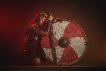 Woman warrior in the armor and with the sword and shield in hands stands on her knees. Lose the...