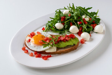 Fototapeta na wymiar Sandwich with cheese, fried egg and avocado for breakfast. Arugula with mozzarella with finely chopped tomatoes.