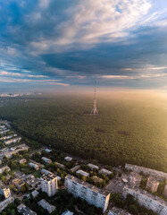 Aerial sunrise morning city view on telecommunication tower in forest near residential district with scenic sun shining in cloudy sky. Kharkiv, Ukraine. Vertical