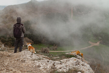 A man and a Pembroke Welsh Corgi climb above the clouds high in the mountains.