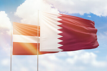 Sunny blue sky and flags of qatar and latvia