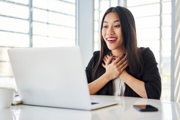Surprised grateful young asian business woman looking at laptop while working at office