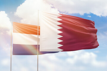 Sunny blue sky and flags of qatar and netherlands