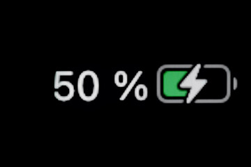 Smartphone charged battery level indicator - charging process - fifty, 50 percent: close up macro view of gadget display, screen, black background. Energy, technology, digital and symbol concept