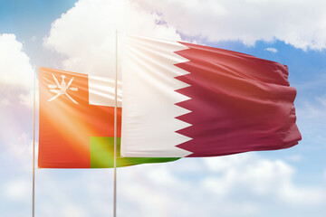 Sunny blue sky and flags of qatar and oman