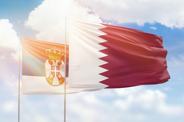 Sunny blue sky and flags of qatar and serbia