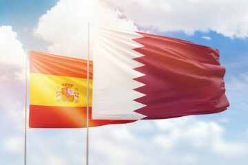 Sunny blue sky and flags of qatar and spain