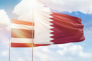 Sunny blue sky and flags of qatar and thailand