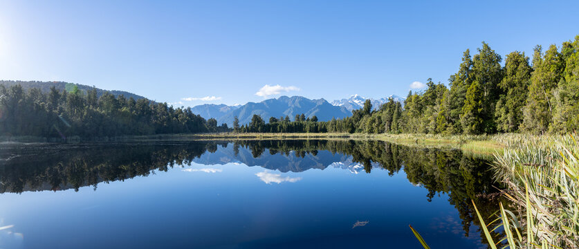 Leading line of forest edge of Lake matheson with Southern Alps and perfect reflection