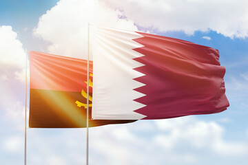 Sunny blue sky and flags of qatar and angola