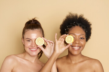 Colorful citrus circles near the face of cheerful multiracial women smiling and holding fresh...