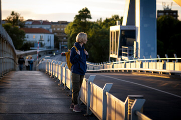 A female tourist with a yellow backpack stands on a metal bridge.
