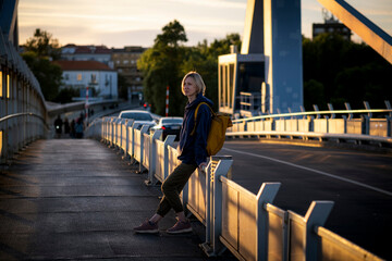 A female with a yellow backpack stands on a metal bridge during sunset. Porto, Portugal.