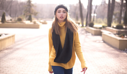 Outdoor photo of beautiful girl with long hair wearing knitted sweater, hat and scarf and posing at spring park