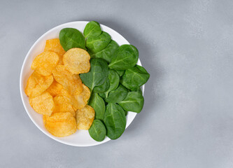 Plate filled with chips and spinach. Concept of healthy and unhealthy food.