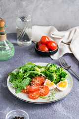 A plate with broccoli, arugula, tomato and boiled egg on a plate on the table. Vertical view