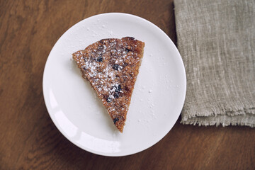 A delicious piece of lemongrass with blueberries and cranberries, without milk and eggs on flaxseed flour. Part of the pie is on a white plate on the table. The concept of healthy eating
