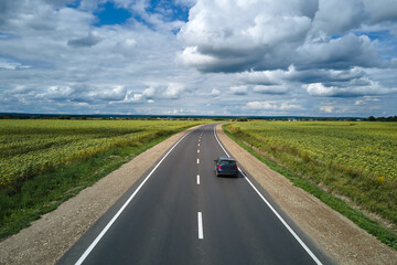 Aerial view of intercity road between green agricultural fields with fast driving car. Top view from drone of highway traffic
