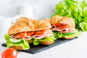 Two croissant sandwiches with ham, cucumbers, tomato and lettuce on a slate. Homemade fast food.