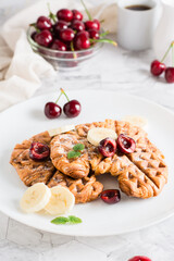 Appetizing croffles with cherries and bananas on a plate. Street food. Vertical view. Close-up