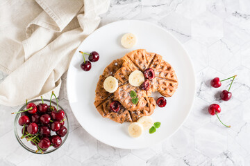 Appetizing croffles with cherries and bananas on a plate on the table. Street food. Top view.