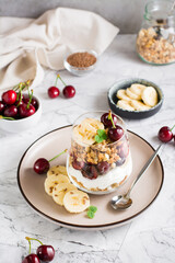 Granola with Greek yogurt, cherry and banana in a glass on the table. Vertical view