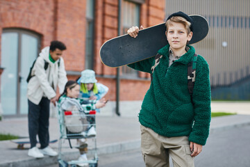 Portrait of skater boy holding his skateboard and looking at camera while standing on street with friends in background © Seventyfour