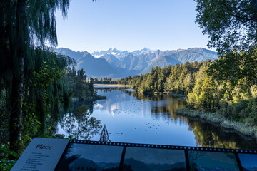 Perfect reflection in Lake Matheson surrounded by beautiful natural forest under blue sky