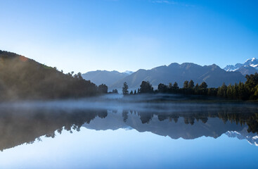 Perfect reflection in Lake Matheson surrounded by beautiful natural forest under blue sky