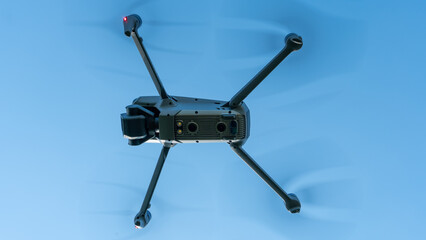 A modern drone against a clear blue sky. The quadcopter hovered motionless in the sky. The use of aircraft for reconnaissance and fire correction.