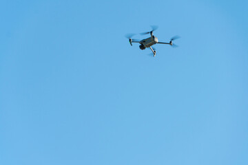 A modern drone against a clear blue sky. The quadcopter hovered motionless in the sky. The use of aircraft for reconnaissance and fire correction.