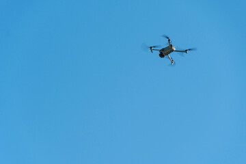 A modern drone against a clear blue sky. The quadcopter hovered motionless in the sky. The use of aircraft for reconnaissance and fire correction.