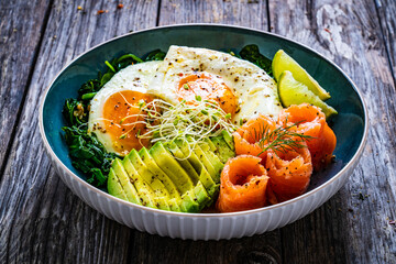 Salmon salad - smoked salmon, sunny side eggs, avocado and spinach on wooden table
