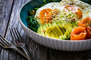 Salmon salad - smoked salmon, sunny side eggs, avocado and spinach on wooden table
