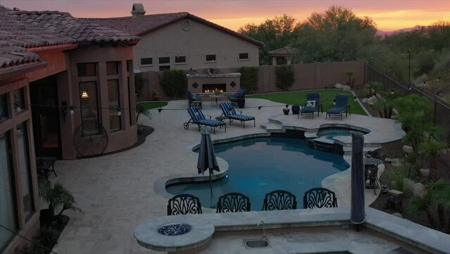 A 4k aerial view of a desert landscaped home in Arizona featuring a travertine tiled pool deck.