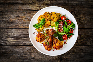Barbecue chicken drumsticks with fried potato, lettuce and mini tomatoes on wooden table
