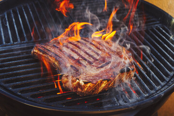 Barbecue dry aged Wagyu cote de boeuf steak grilled as close-up on a charcoal grill with fire and...