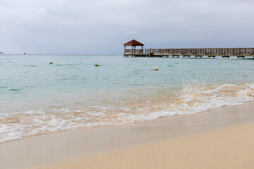 A pier goes into the sea,at the end there is a gazebo.The blue sea water and the sky are separated by the horizon line,a pier.Caribbean Coast in the Dominican Republic.A wave runs over the sandy shore