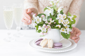 Beautiful composition with delicious French macarons and spring flowers in a white cup. Young beautiful girl in a lace dress holding a plate with sweet dessert and apple tree flower. Bride's morning