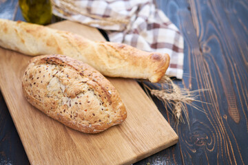 Fresh bread loaf and baguette on wooden cutting board at kitchen table