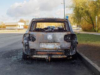 Close rear view to the burned car on the street during the day. Selective focus on burned engine.