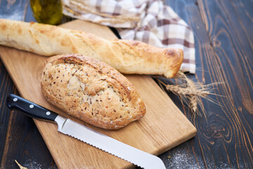 Fresh bread loaf and baguette on wooden cutting board at kitchen table