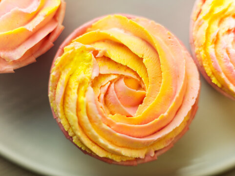 Directly from above top view of handmade cupcake with pink yellow whipped butter cream made as rose flower, closeup background