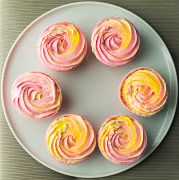 Closeup top view of six fresh handmade cupcakes with pink yellow cream placed on plate. Sweet candy bar background