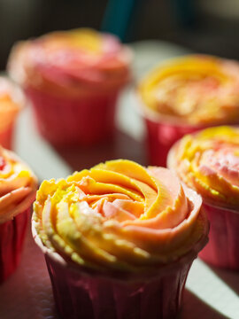 Closeup of freshly made cupcake decorated with pink yellow buttercream frosting. Vertical selective focus background