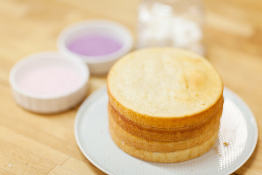 Sponge layers for cake on plate and defocused sugar beads in saucers on table. Bakery and cooking background