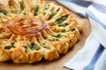 Delicious pie with spinach and ricotta cheese in the shape of a sunflower, towel next to it, close-up.