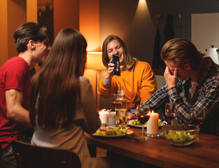 Laughing young woman showing funny selfie of her boyfriend to him and couple of friends during double date dinner at home