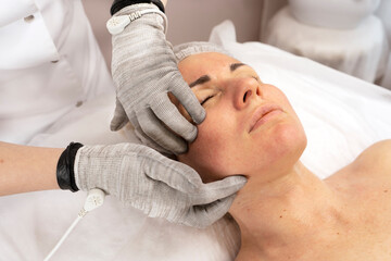 Obraz na płótnie Canvas Electric micro-current procedure for face with conductive gloves. Anti-age concept. Skincare, lifting, spa beauty treatment.